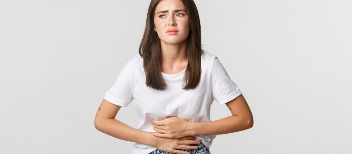 Woman having stomach ache, bending and holding hands on belly, discomfort from menstrual cramps.
